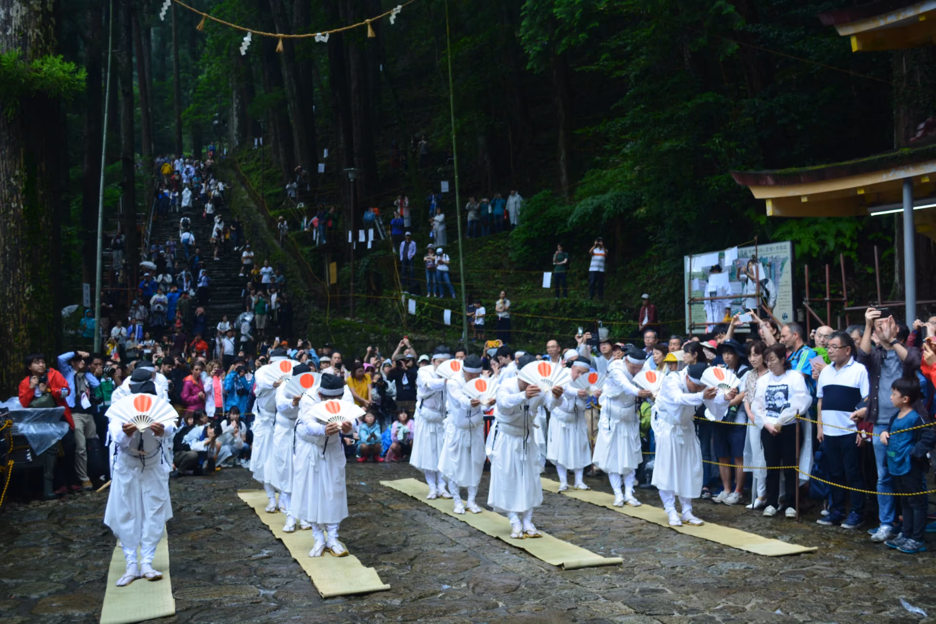 Priests in white bow with rising-sun fans before the crowds at the Nachi Fire Festival, Wakayama
